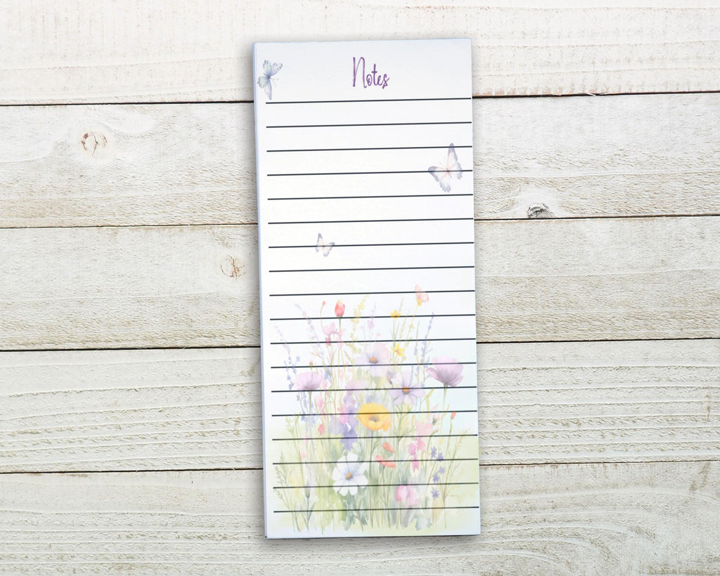 A lined notepad with a floral design on the cover, placed on a wooden surface.
