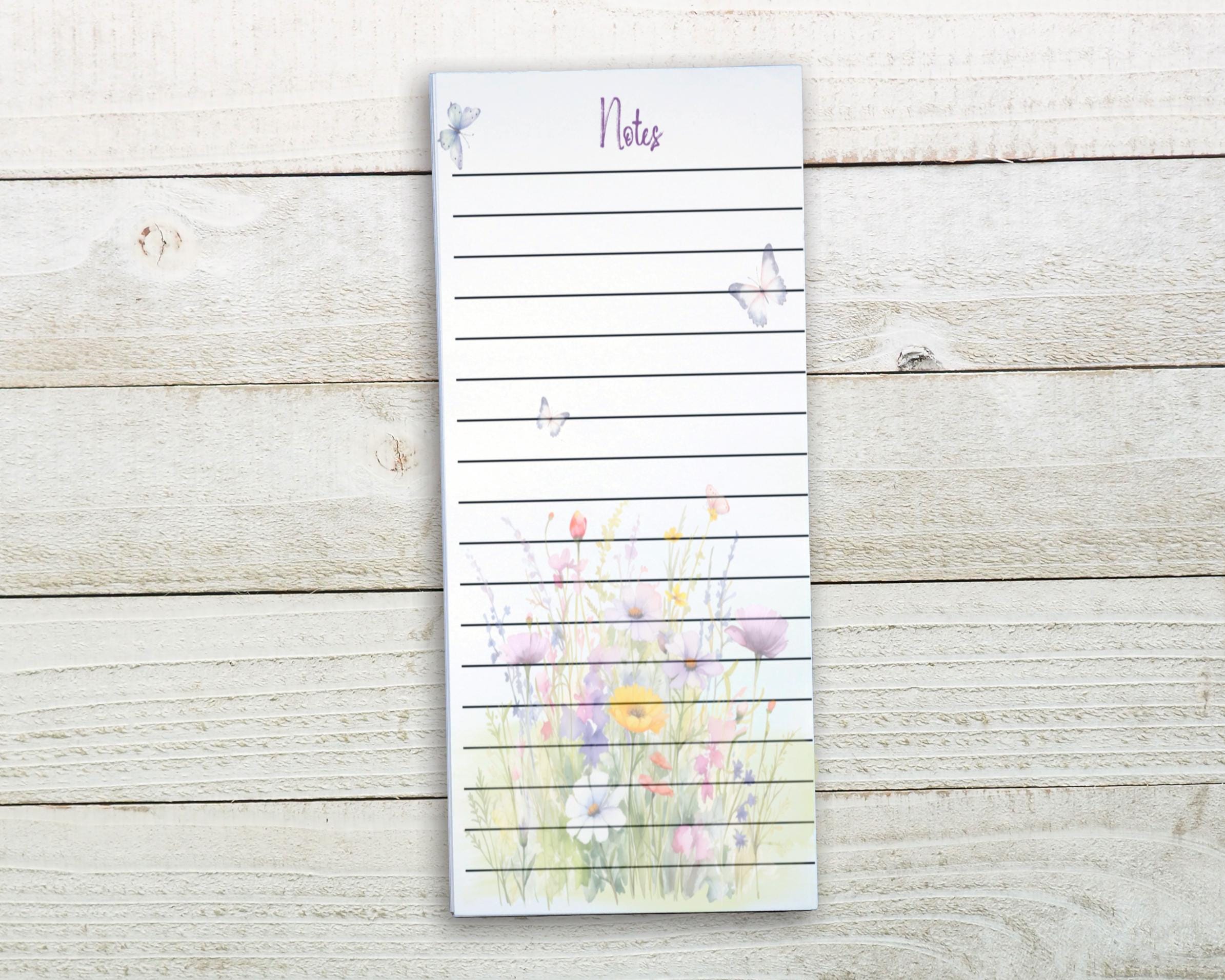 A lined notepad with a floral design on the cover, placed on a wooden surface.