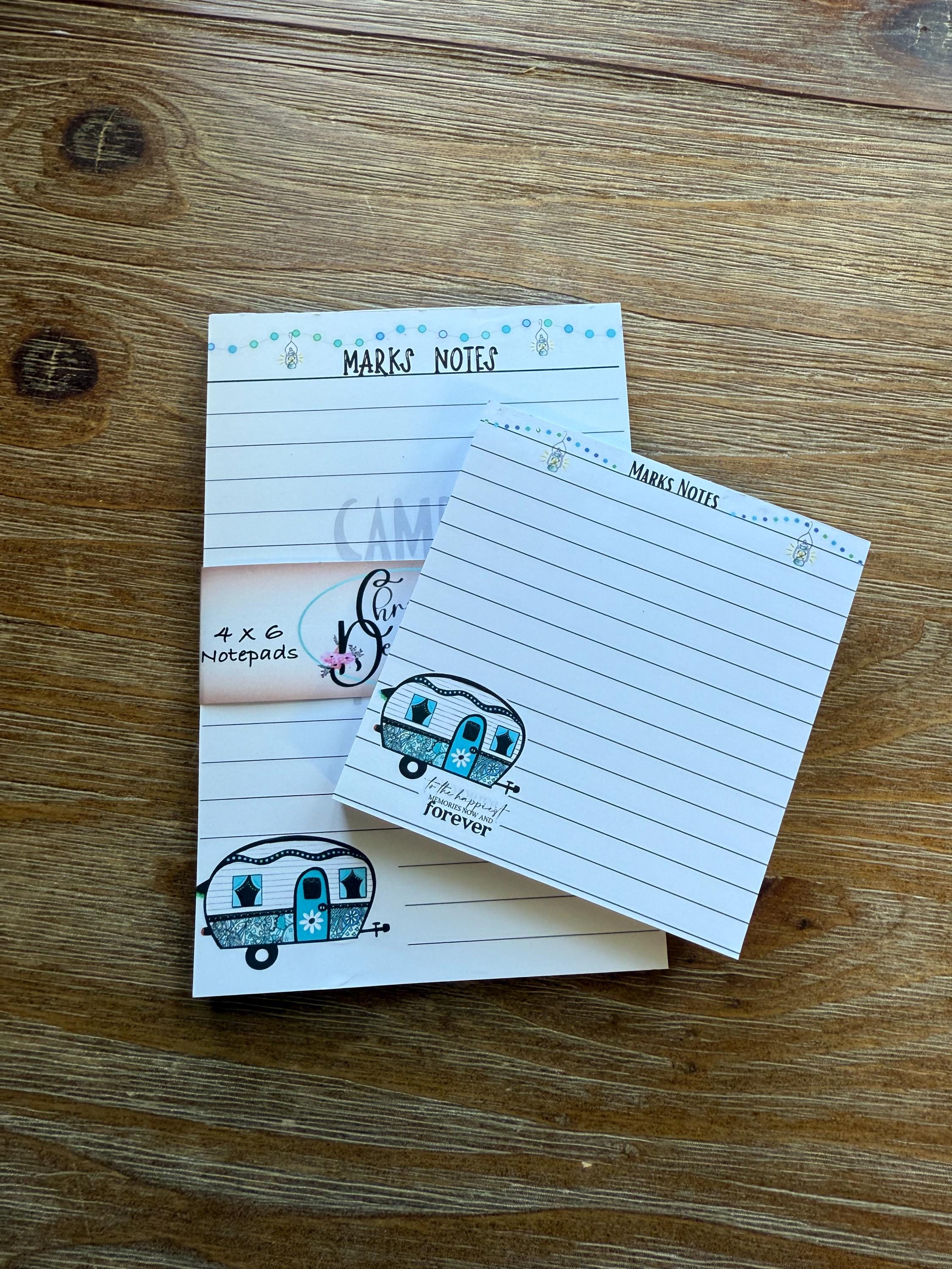 a wooden surface with two lined paper pads and a small decorative item, possibly a piece of paper or a small toy.