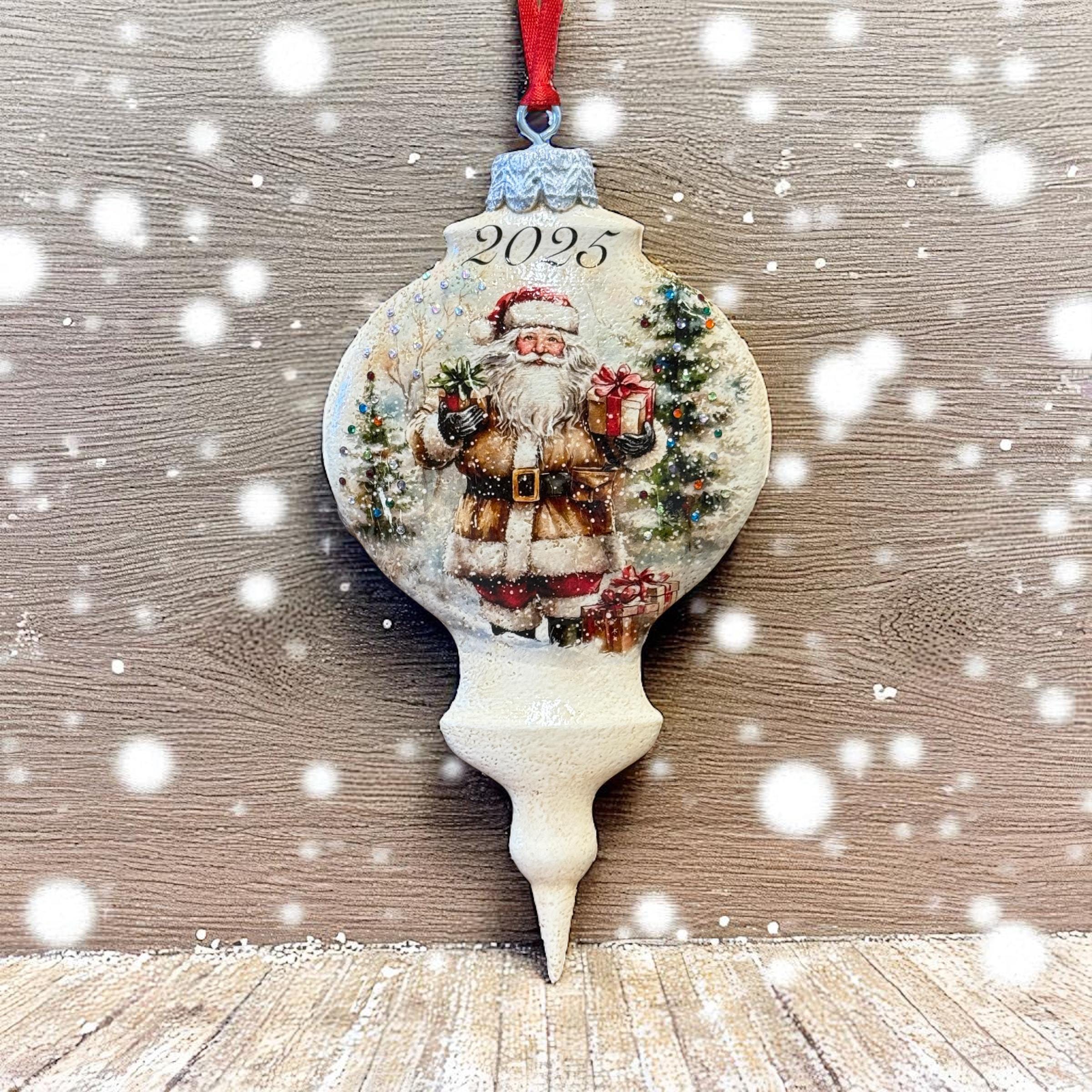 A Christmas ornament with a Santa Claus figure and the year "2025" on it, hanging against a snowy background.