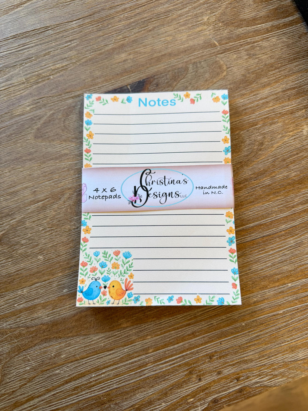 A colorful and decorative notepad with lined pages and a floral border, placed on a wooden surface.