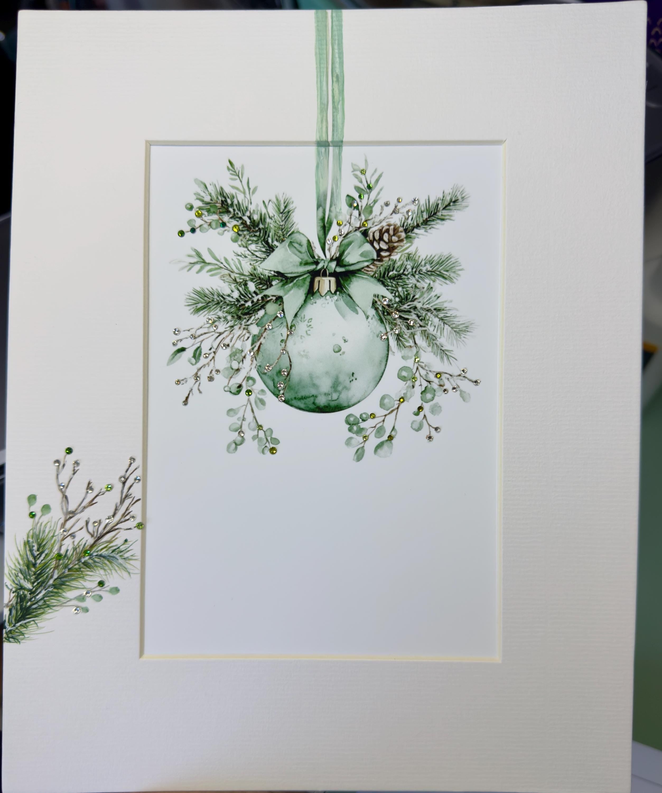 A framed print depicting a Christmas ornament with a bow and greenery, hanging on a white background.
