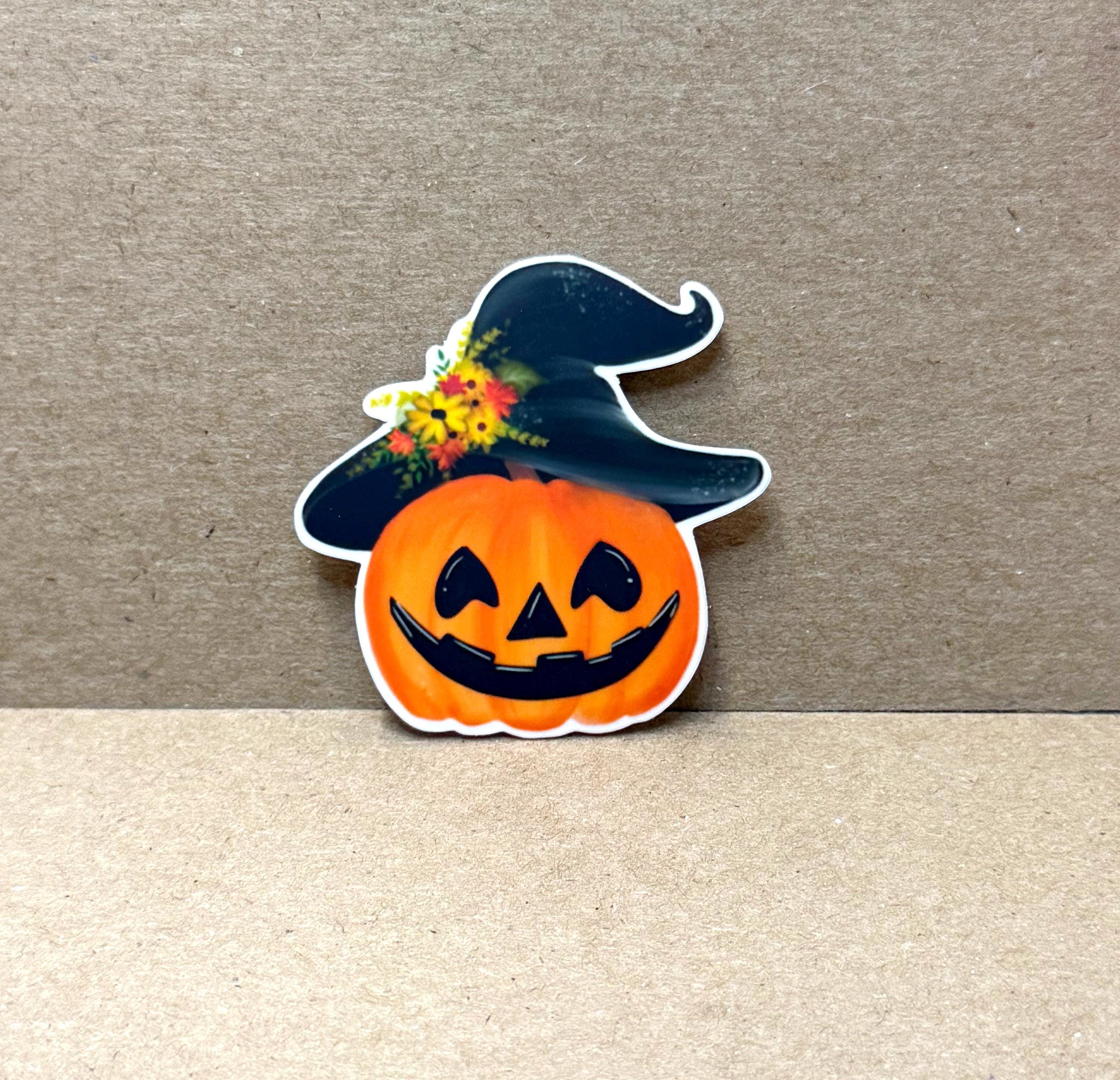 A Halloween-themed pumpkin sticker with a black witch's hat and a flower on top, placed on a brown surface.