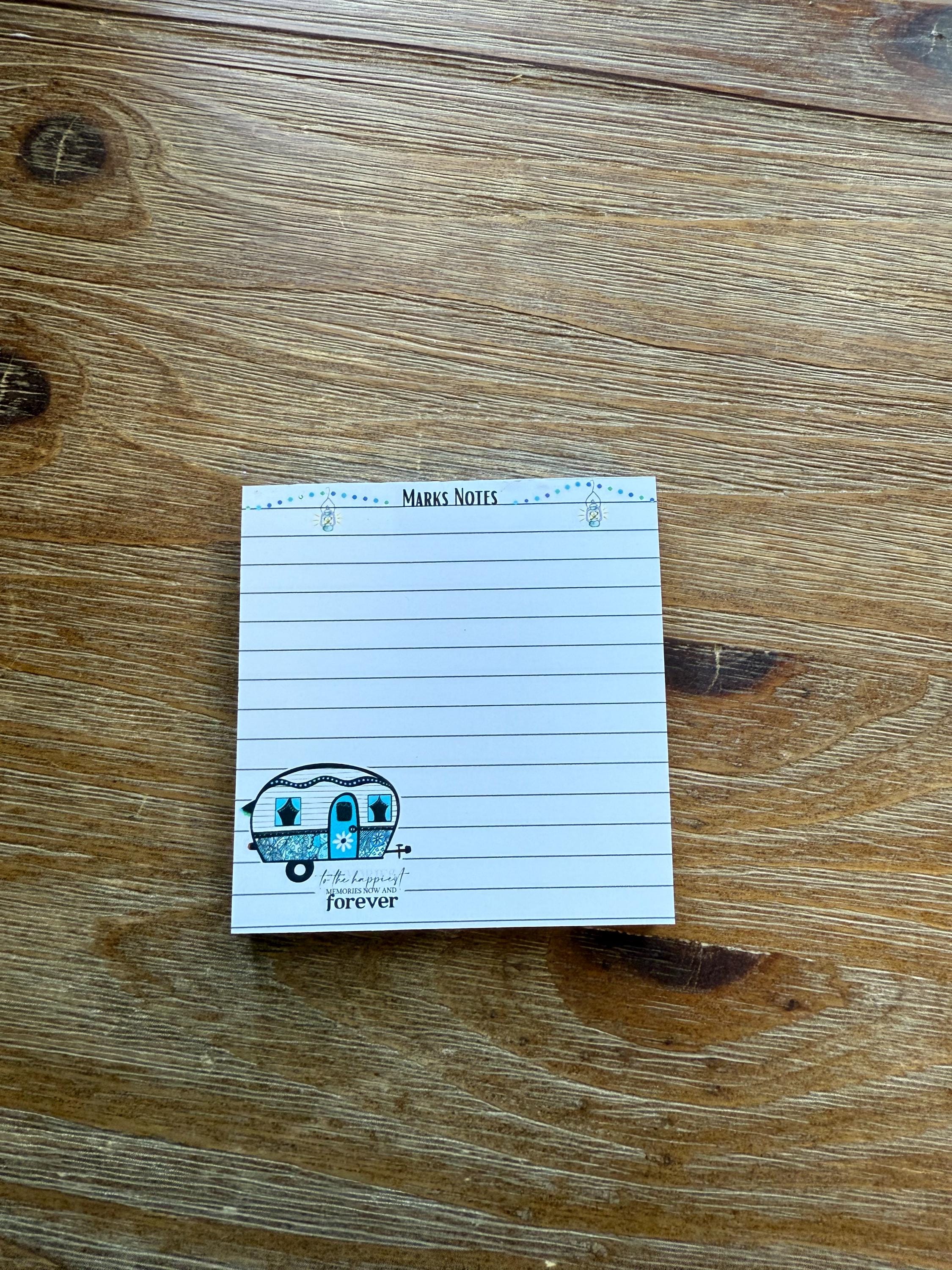A lined notepad with a cartoon image of a blue and white camper van on the cover, placed on a wooden surface.