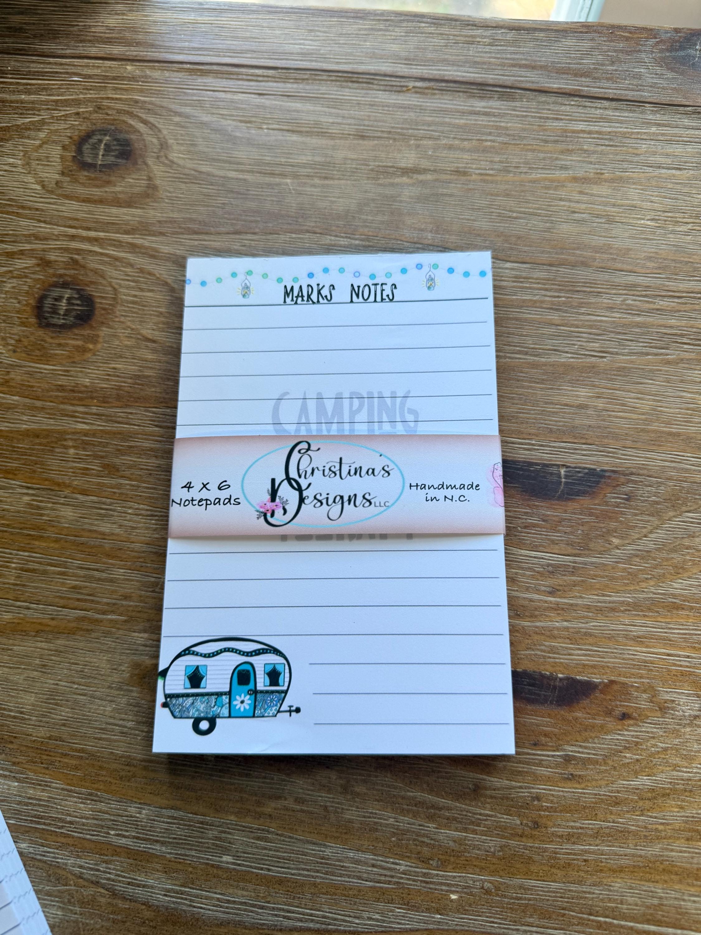 A white lined notepad with a decorative border and a small illustration of a camper on the right side, placed on a wooden surface.