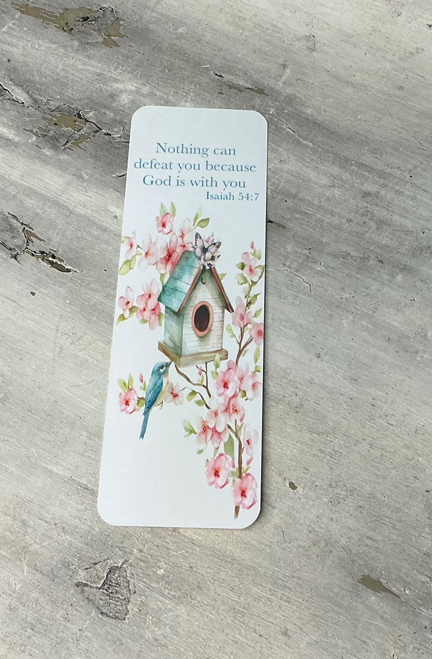 A white bookmark with a floral design and a birdhouse illustration, placed on a wooden surface.