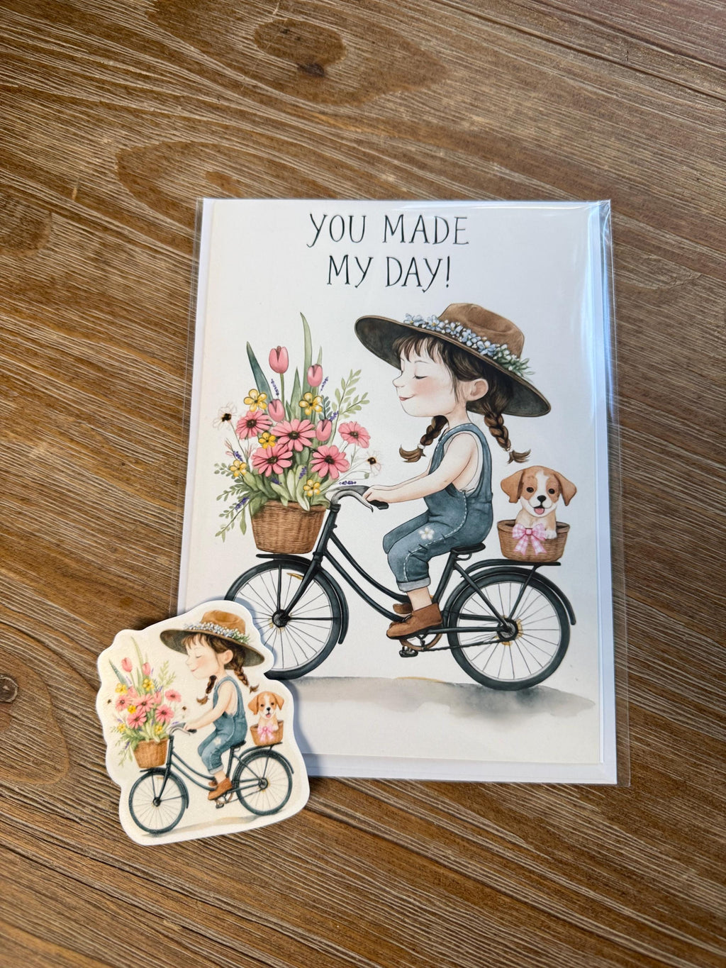 a greeting card with a girl riding a bicycle and a sticker depicting a girl riding a bicycle with flowers in a basket.