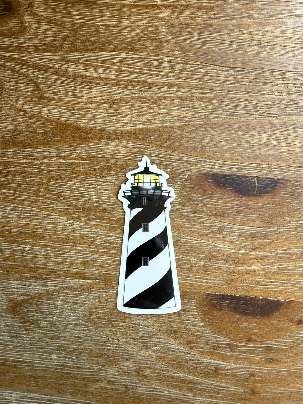 A sticker of a lighthouse is placed on a wooden surface.