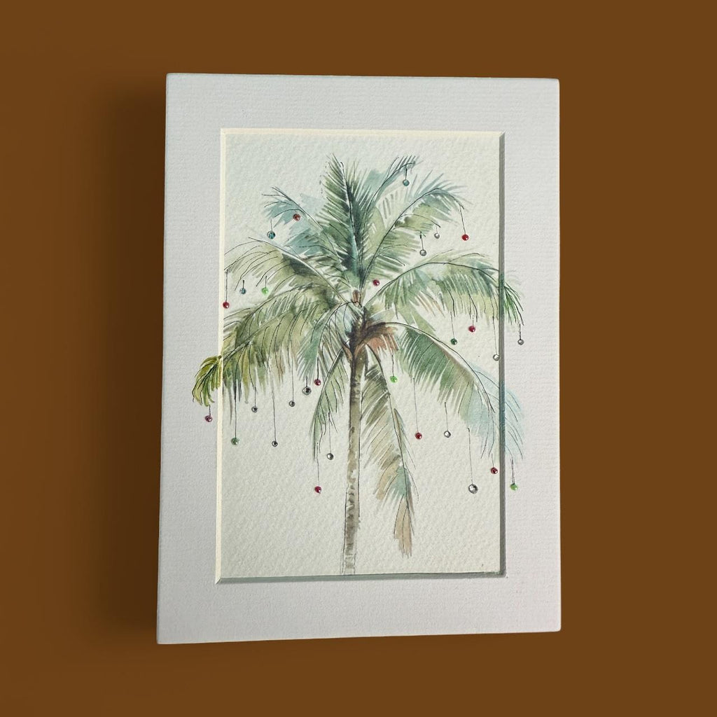 A framed watercolor painting depicting a palm tree with green leaves and red ornaments hanging from its branches.