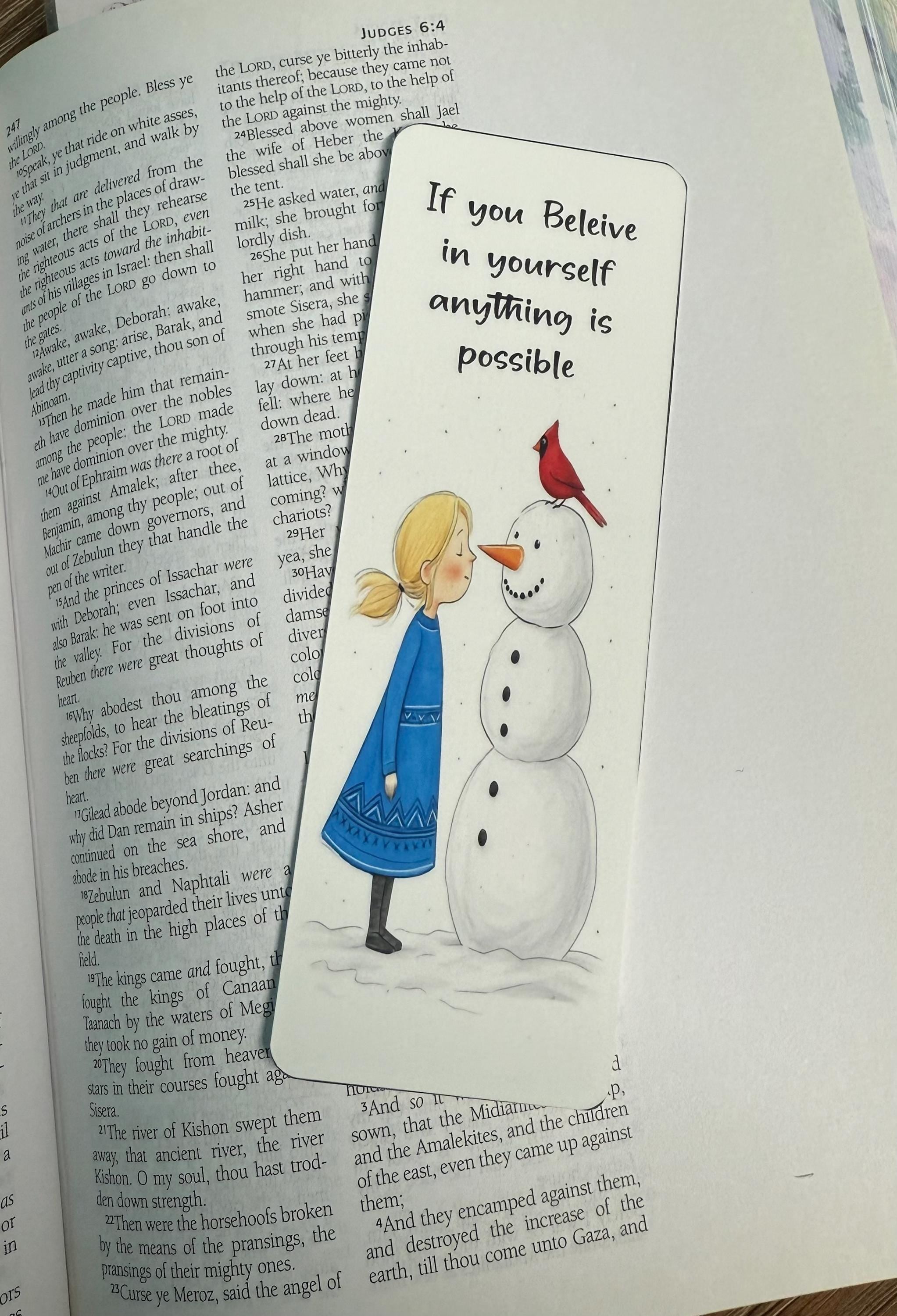 a bookmark with an illustration of a young girl standing next to a snowman, with a red bird perched on the snowman&#39;s head. The text on the bookmark reads &quot;If you Believe in yourself anything is possible&quot;.