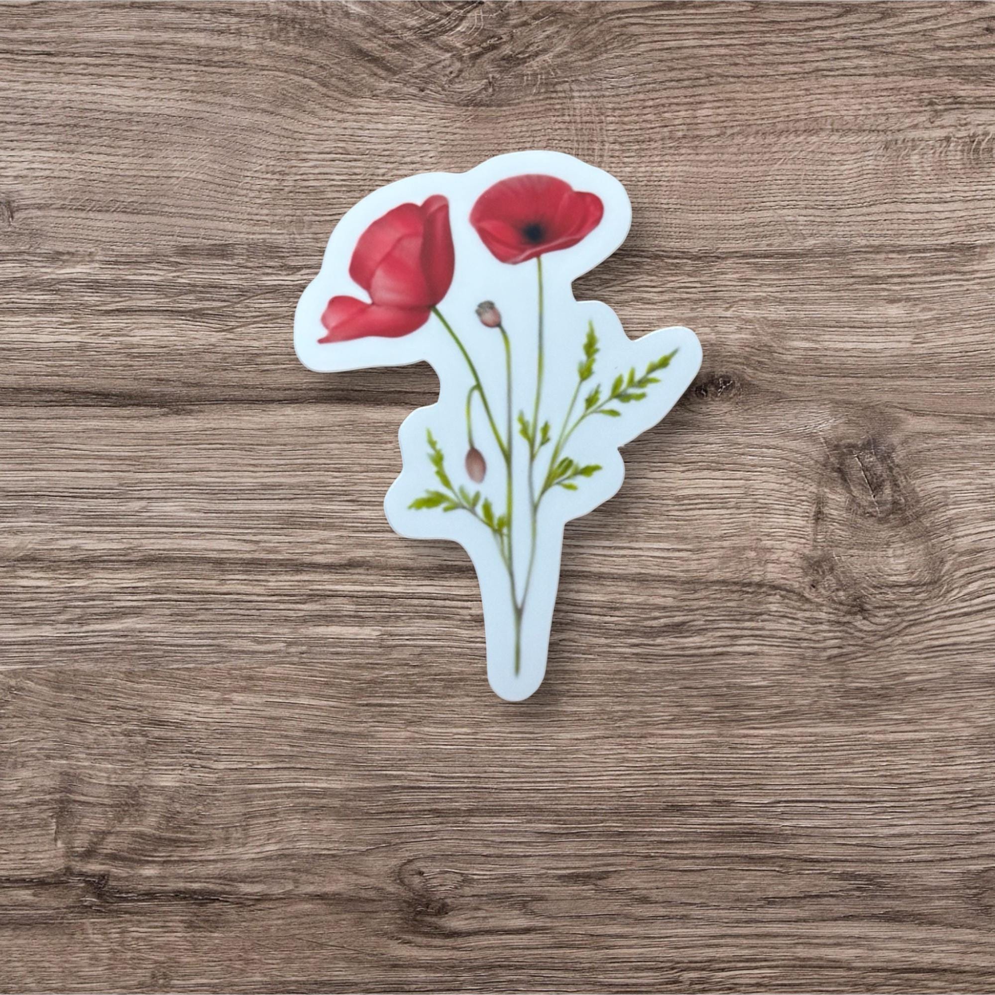 A sticker depicting two red poppies with green leaves is placed on a wooden surface.