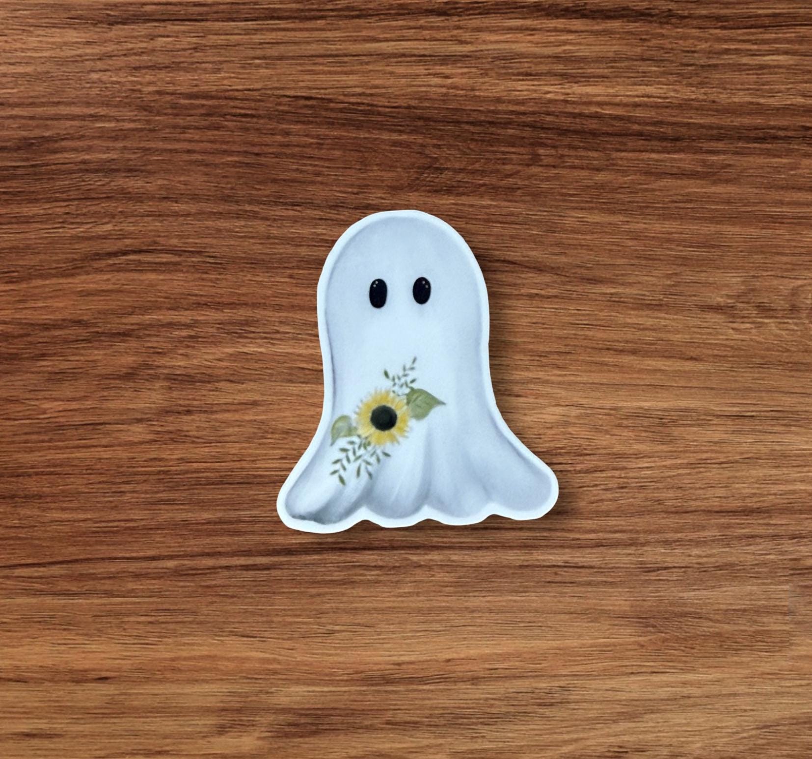 A white ghost with a flower on its chest is sitting on a wooden surface.