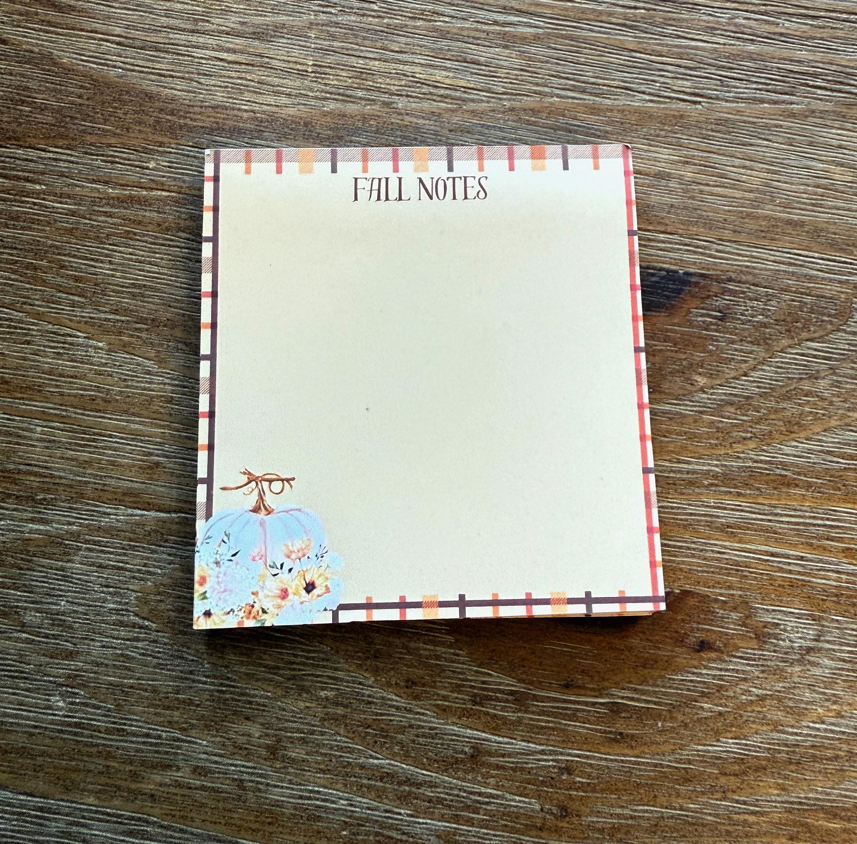 A white sticky note with a floral design and the text "FALL NOTES" printed on it, placed on a wooden surface.