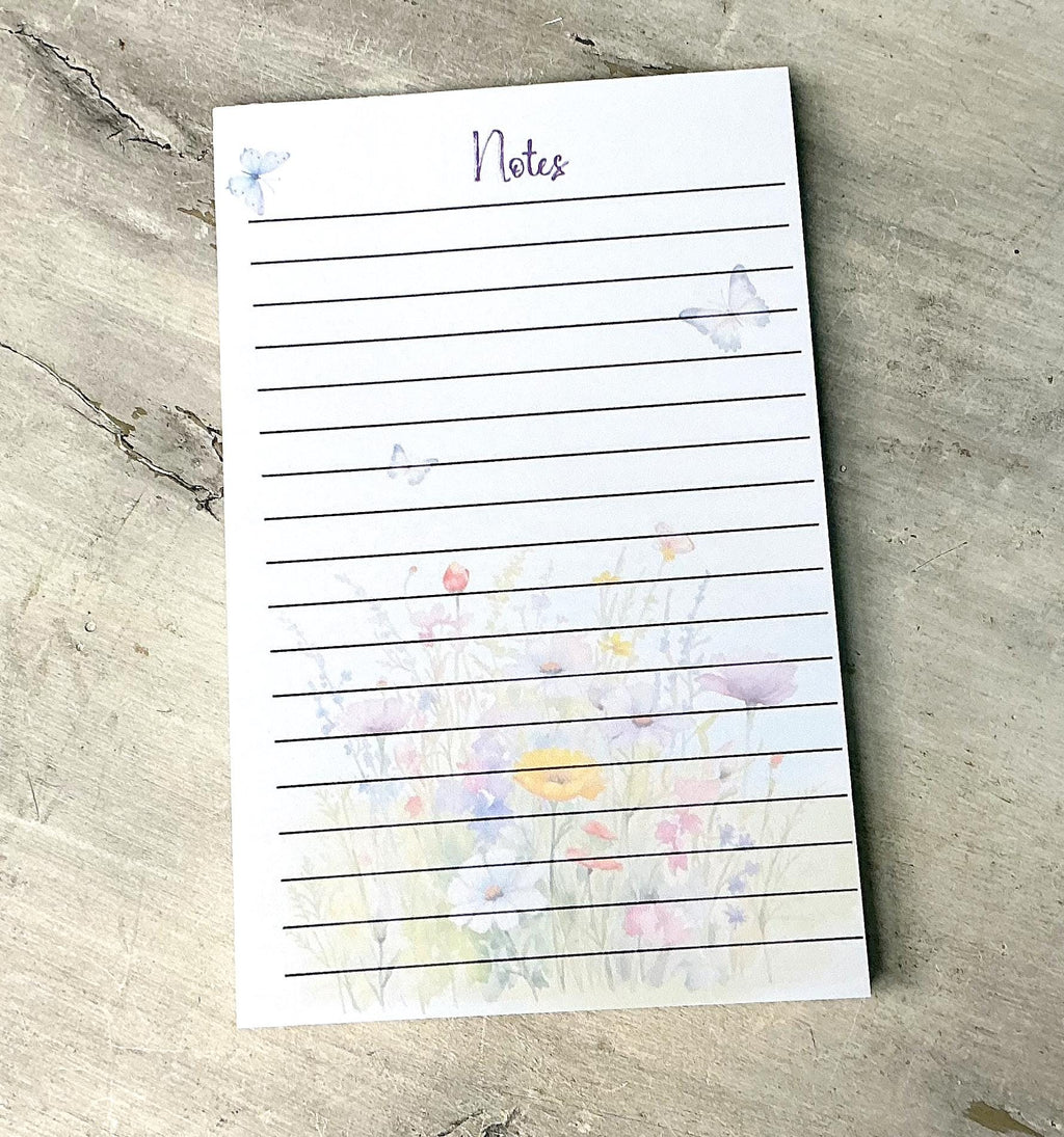 A lined notepad with a floral design on the cover, placed on a textured surface.