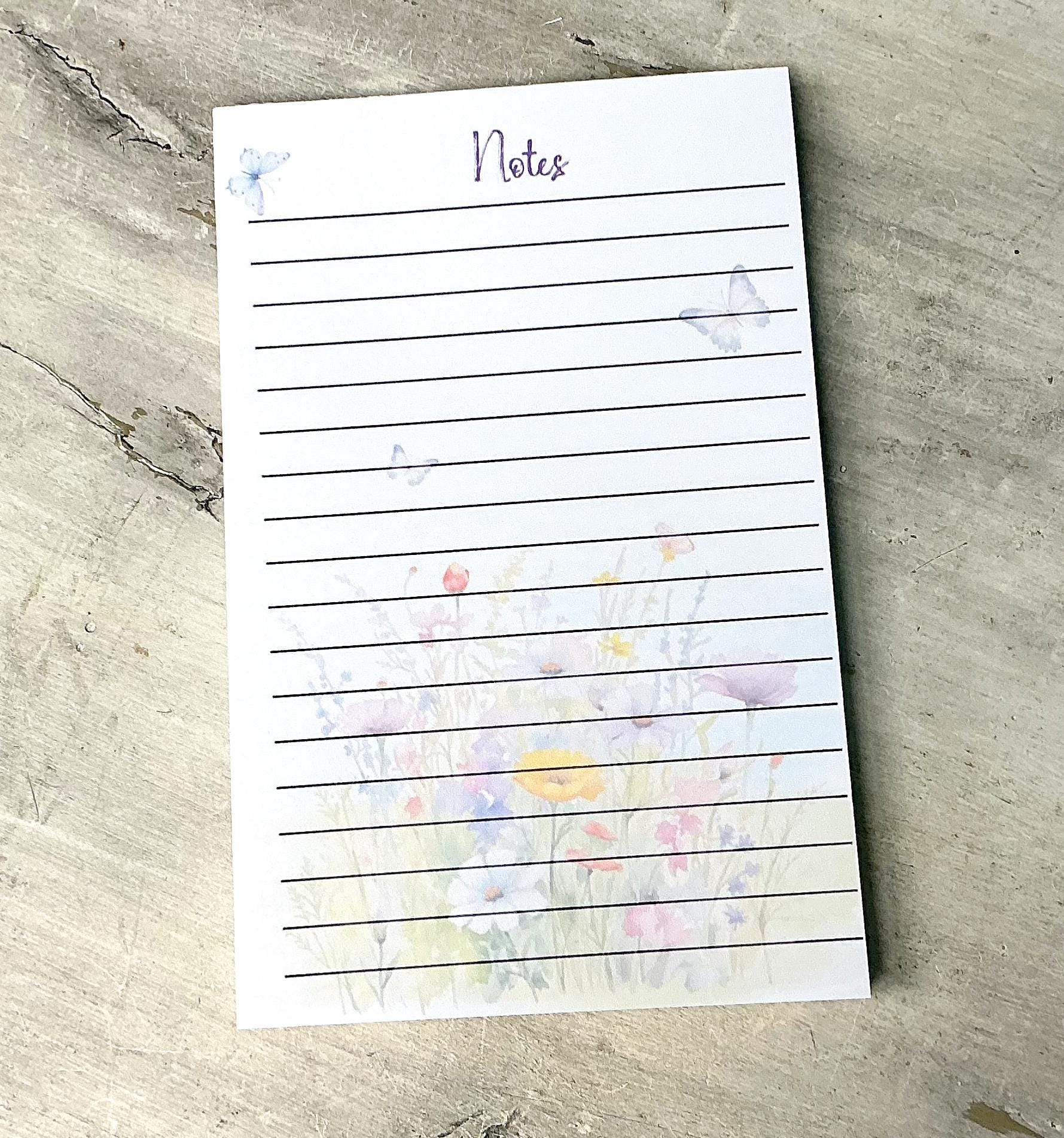 A lined notepad with a floral design on the cover, placed on a textured surface.