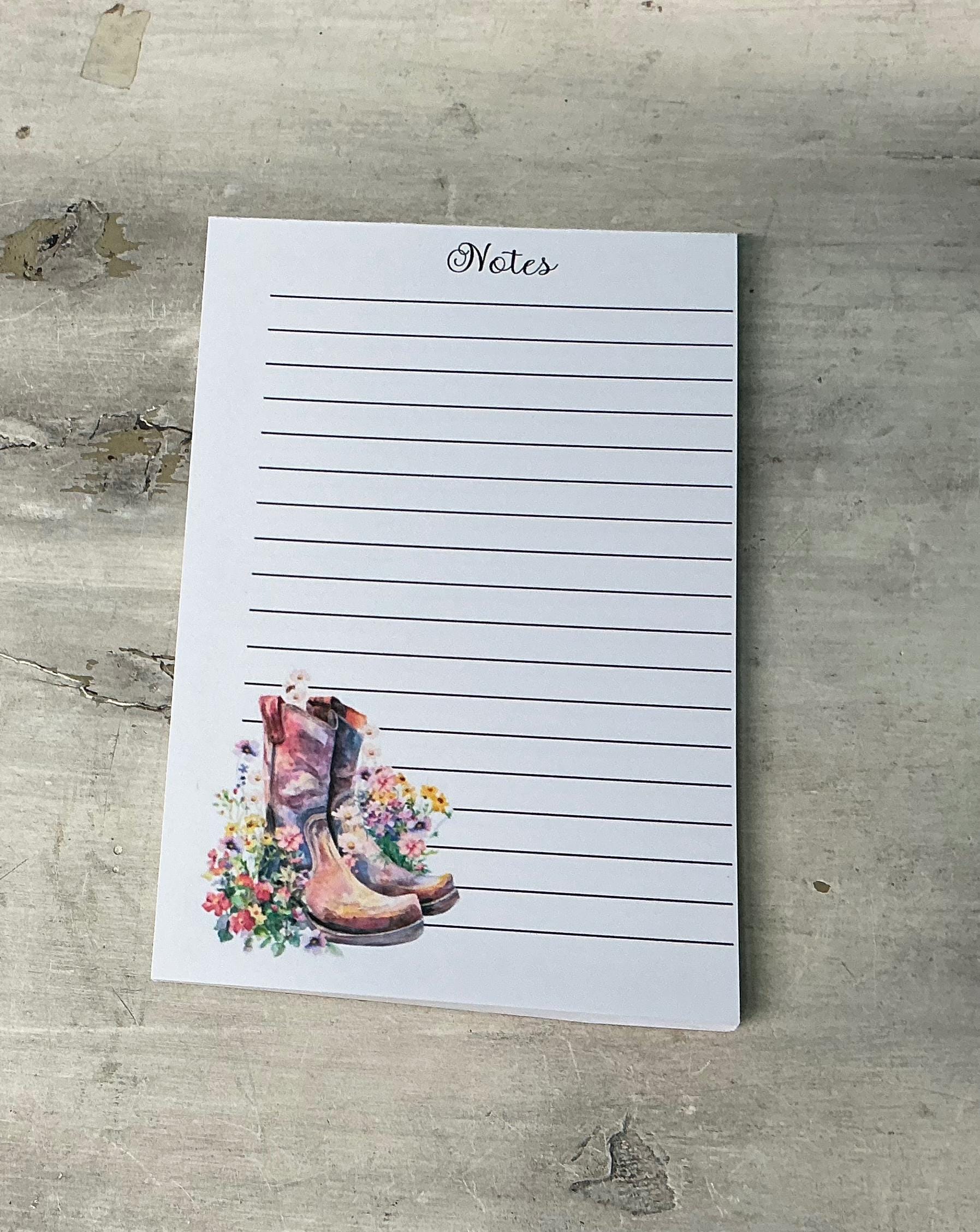 A lined notepad with a printed image of a pair of colorful boots on the cover, placed on a wooden surface.