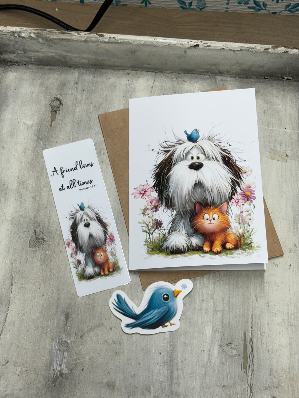 a greeting card with a dog and a cat, along with a small bird-shaped sticker, all placed on a wooden surface.