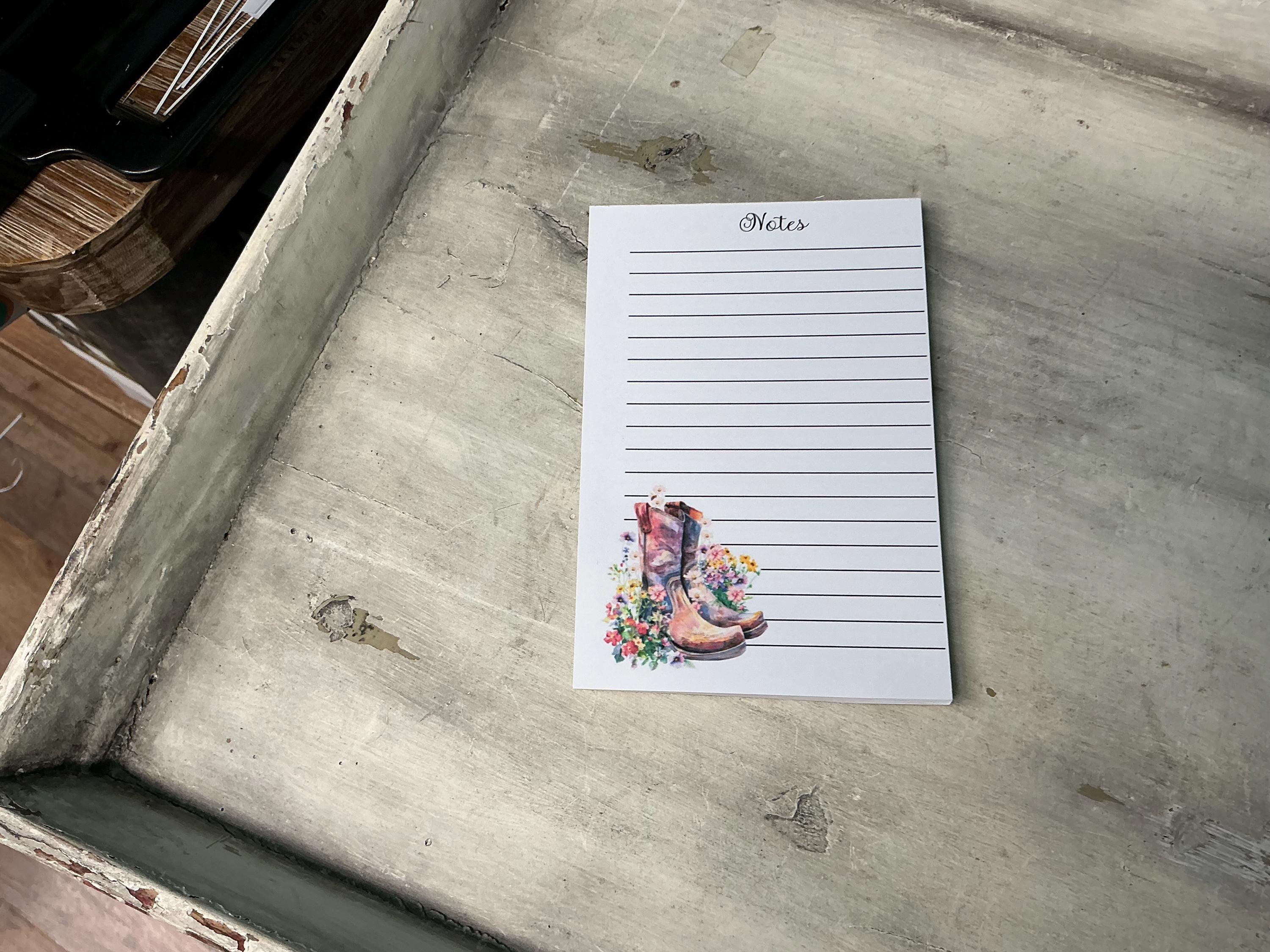 A lined notepad with a printed image of a pair of colorful boots on the cover, placed on a wooden surface.