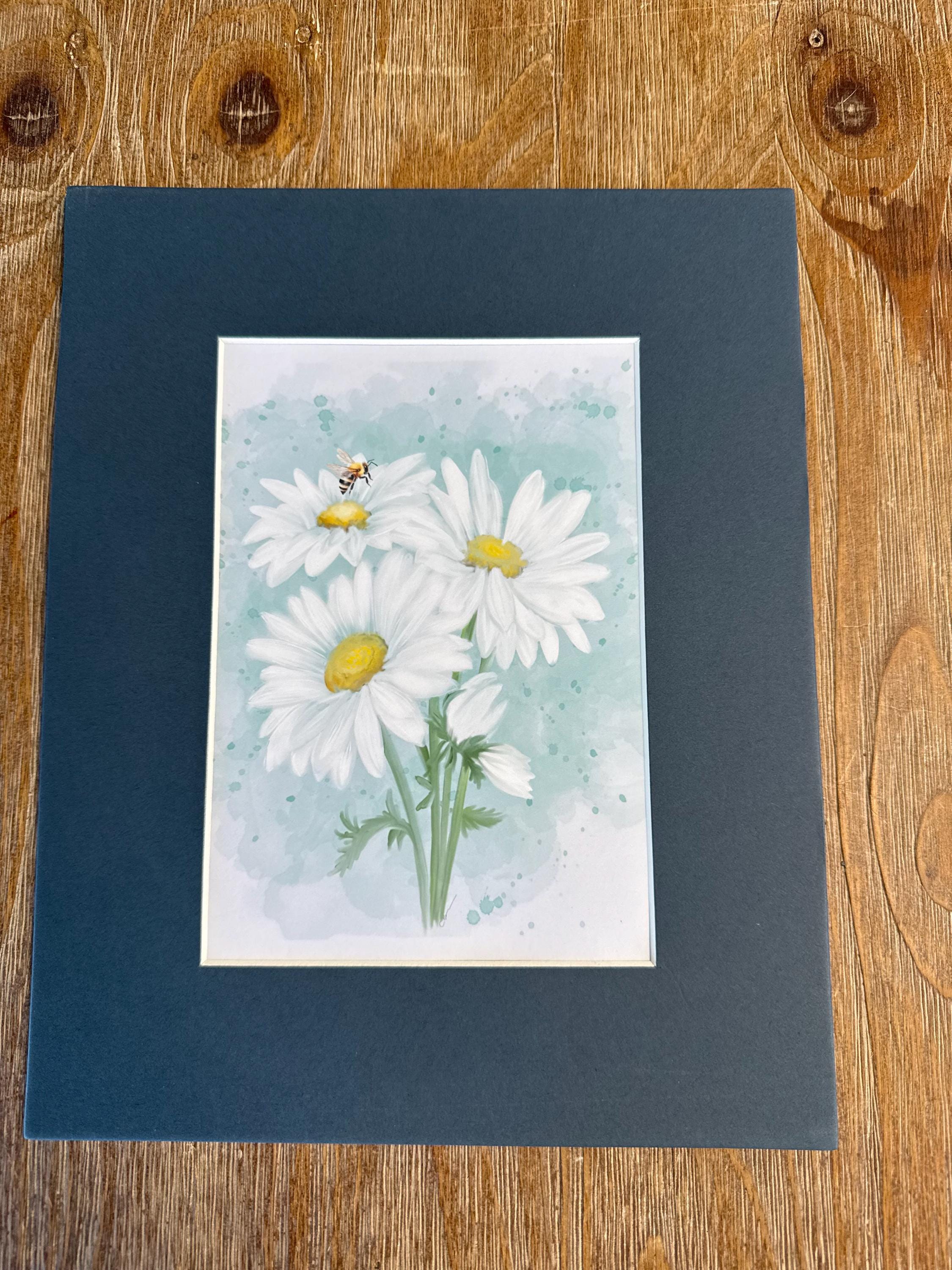 a framed print of a watercolor painting of white daisies with yellow centers, set against a light blue background.