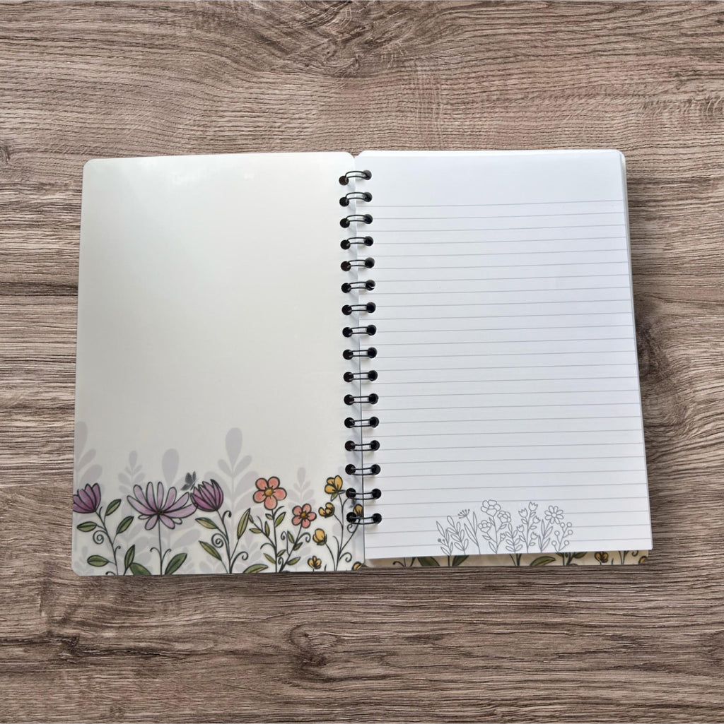 An open spiral-bound notebook with a blank page on the right side, featuring a floral design on the left side.