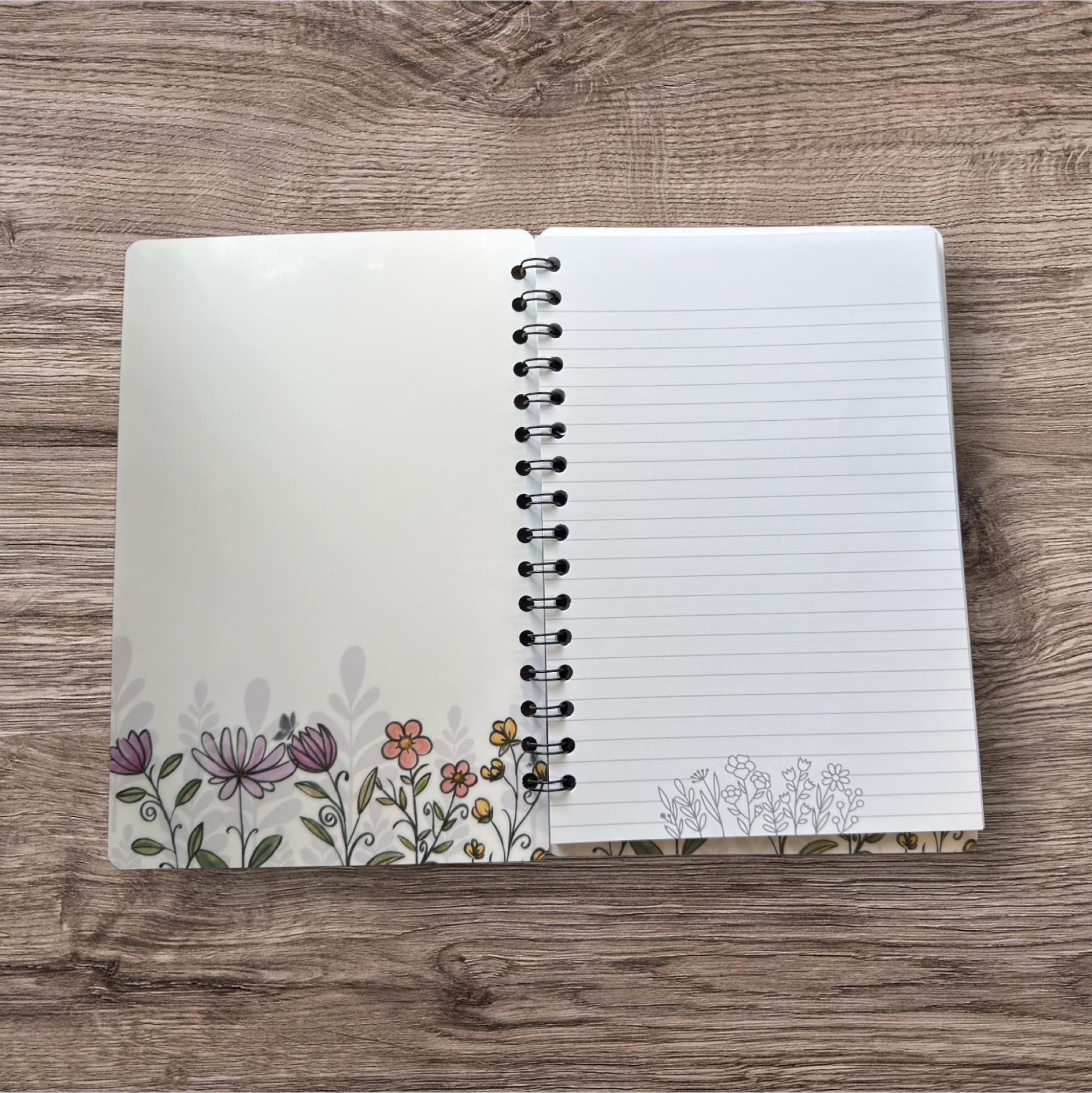 An open spiral-bound notebook with a blank page on the right side, featuring a floral design on the left side.
