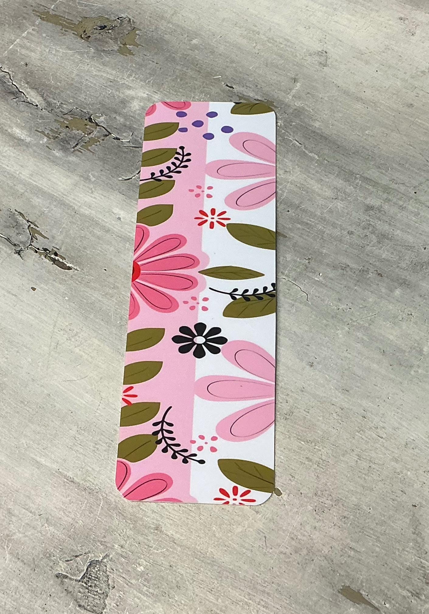 A colorful, floral-patterned bookmark or ruler lying on a concrete surface.