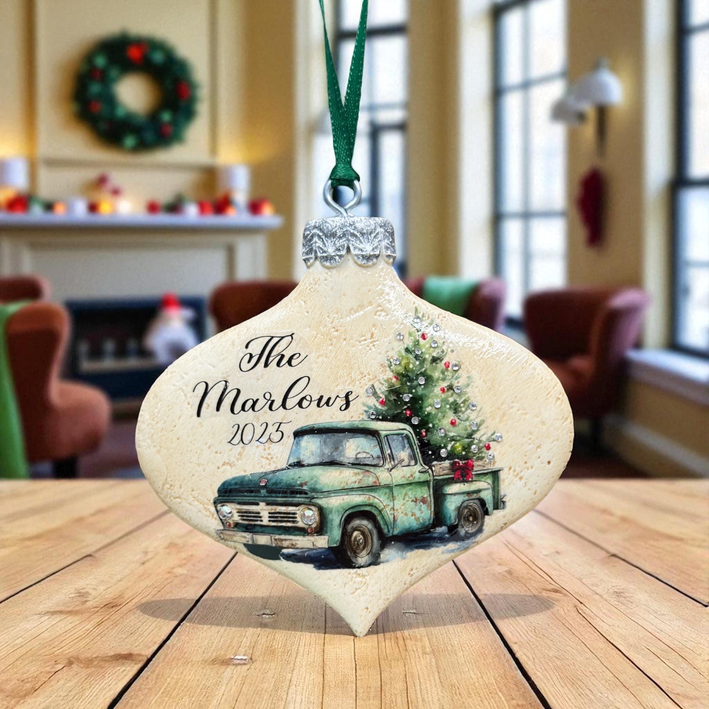 A Christmas ornament featuring a vintage green truck with a Christmas tree on the back, placed on a wooden table.