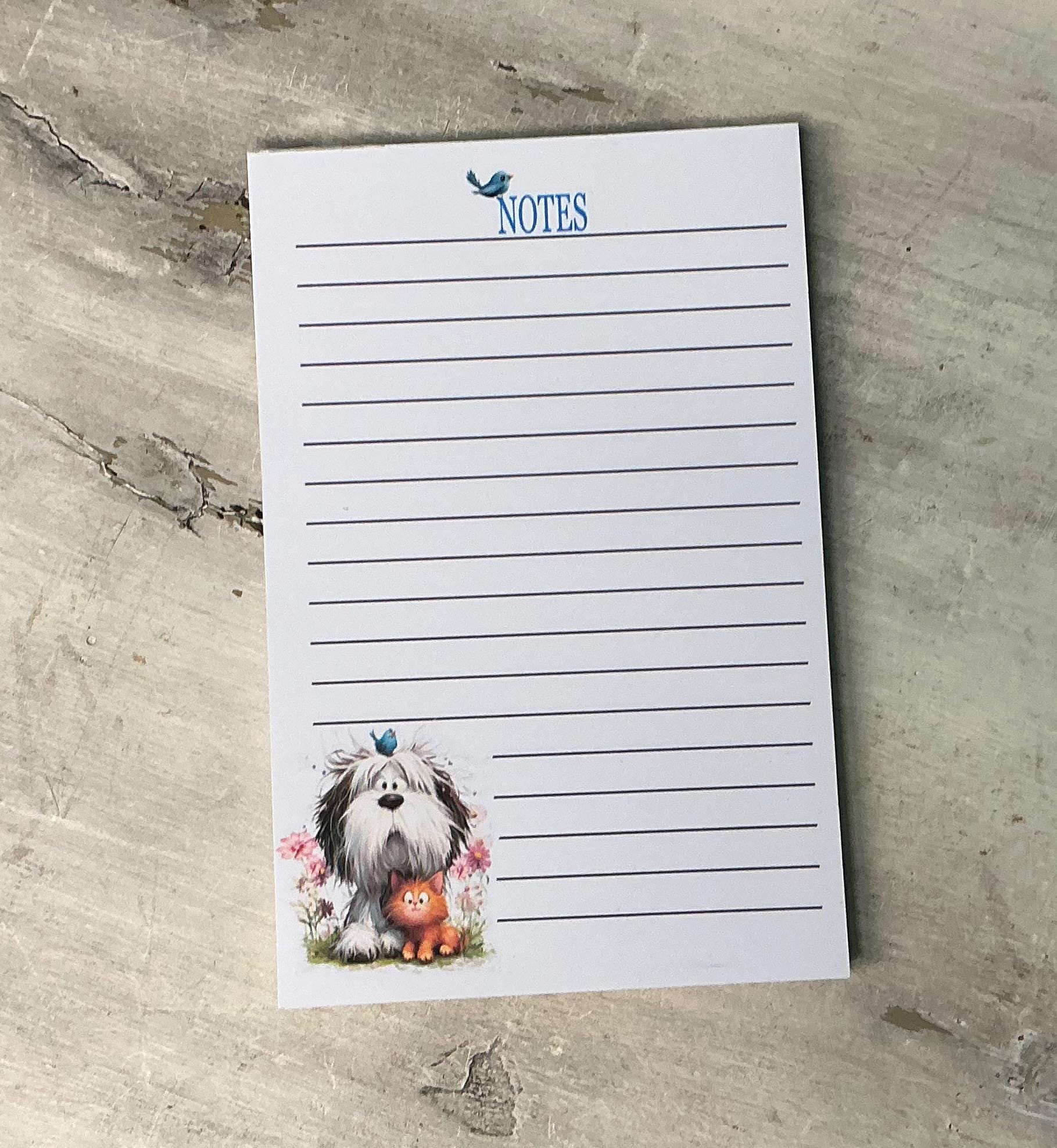 A lined notepad with a cute illustration of a dog and a cat on the side, placed on a wooden surface.