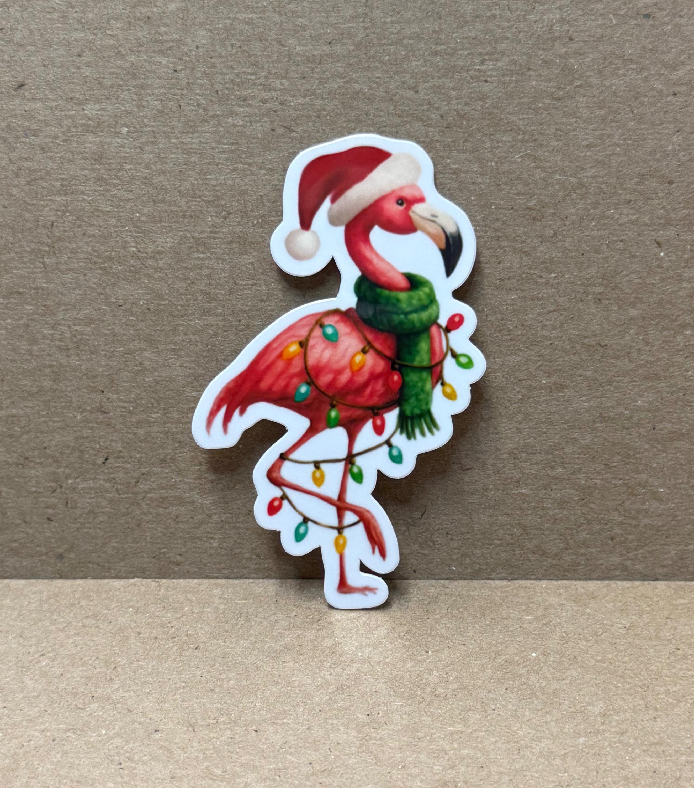 A sticker depicting a flamingo wearing a Santa hat and scarf, with Christmas lights around its neck.