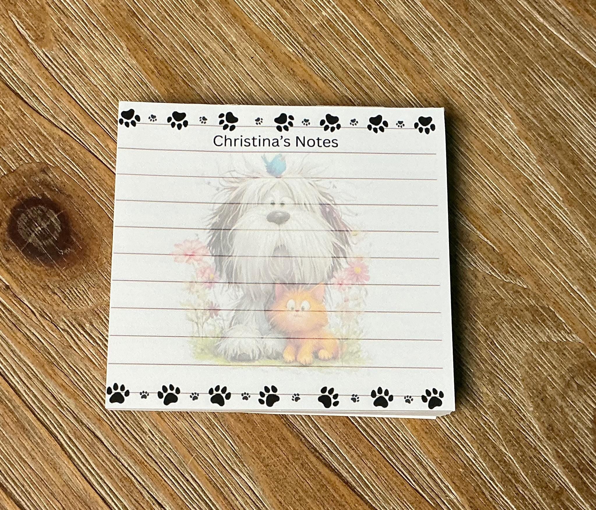A white lined notepad with a dog and cat illustration on the cover, placed on a wooden surface.