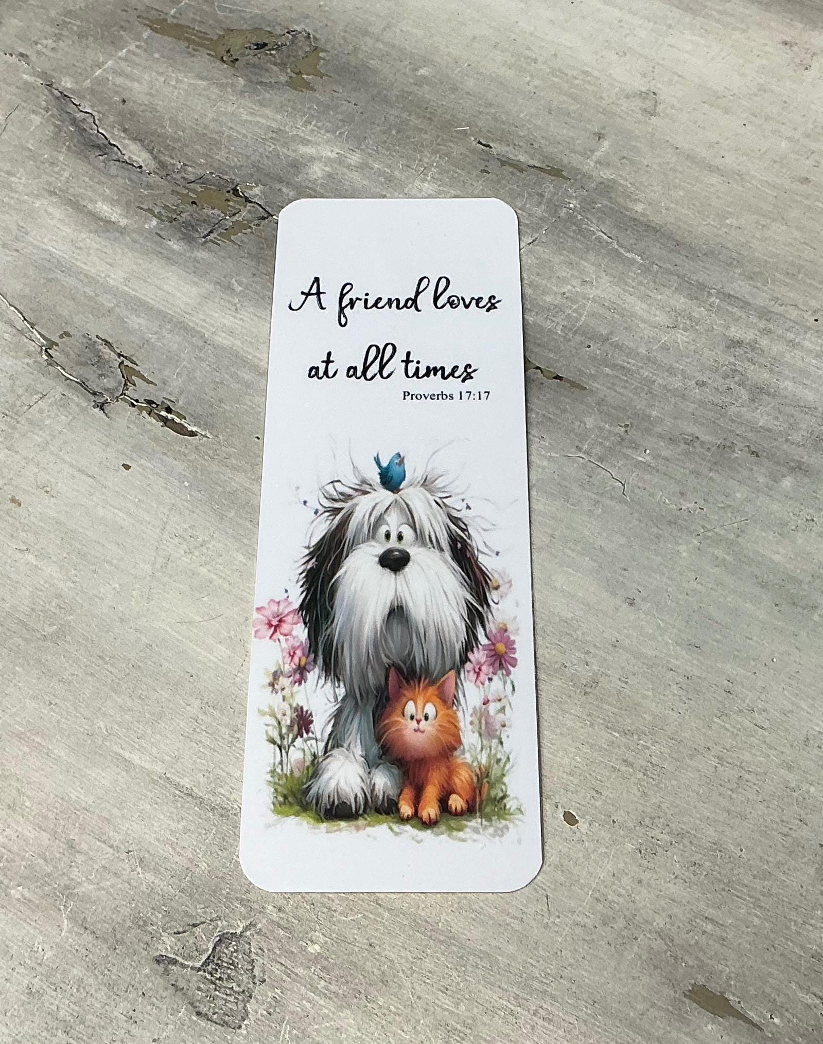 A white bookmark with a black border and illustrations of a dog and a cat sitting together in a grassy area with flowers.